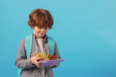 Photo of Cute little boy with lunch box on light blue background. Space for text