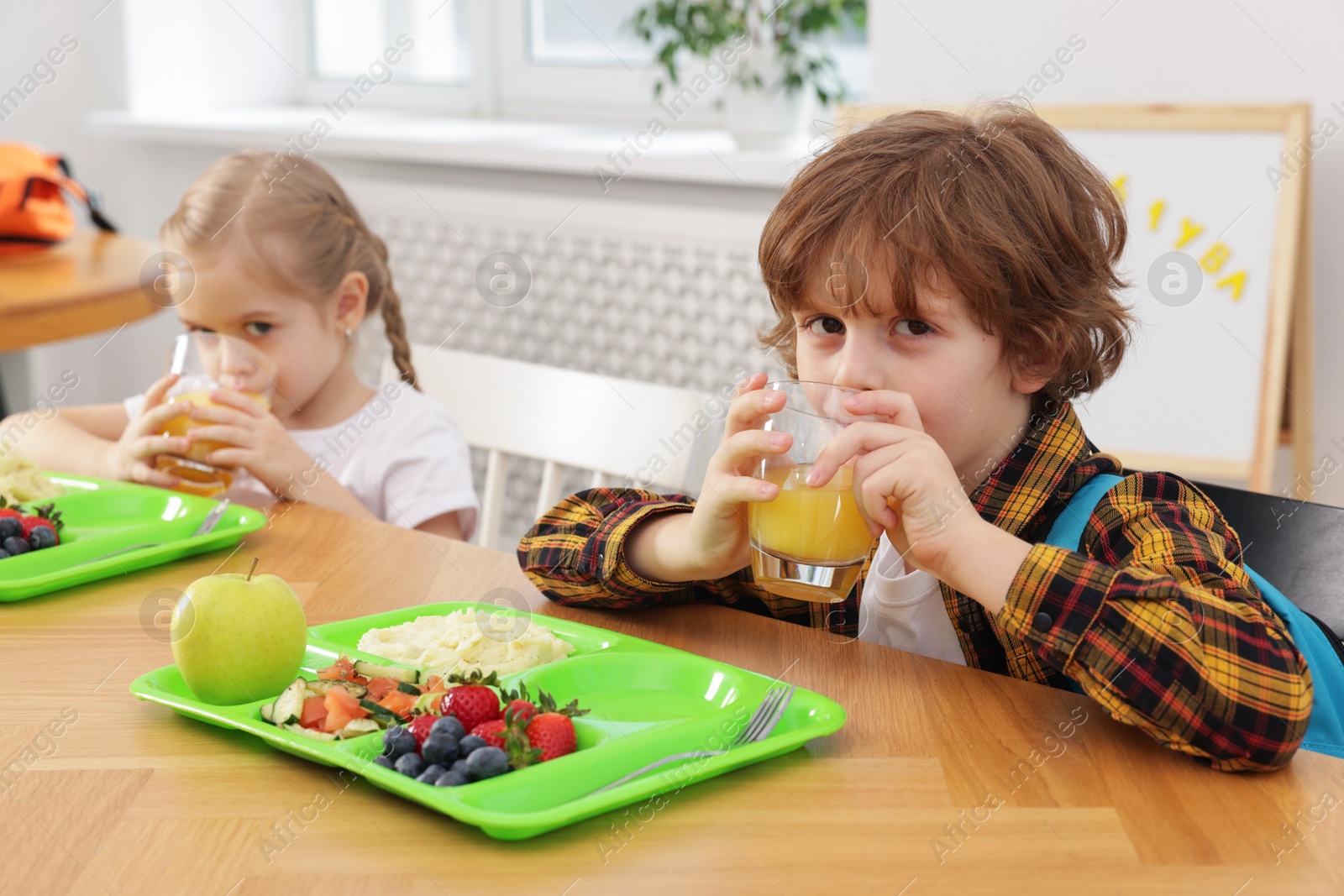 Photo of Cute little children eating lunch at wooden table in school