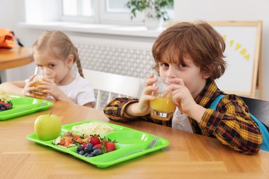 Cute little children eating lunch at wooden table in school