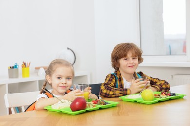 Cute little children eating lunch at wooden table in school