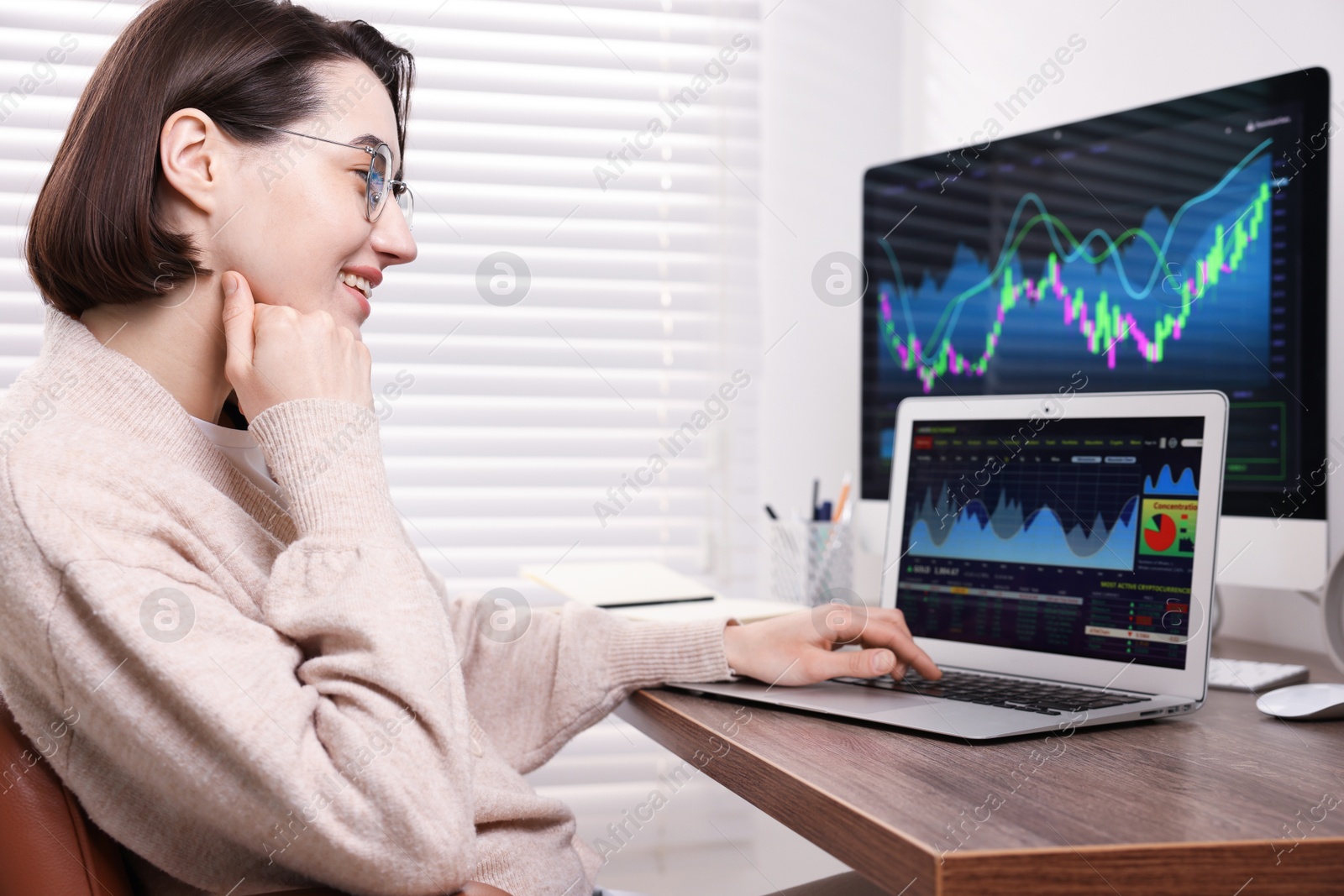 Photo of Stock exchange. Woman analysing financial market on laptop at wooden table indoors