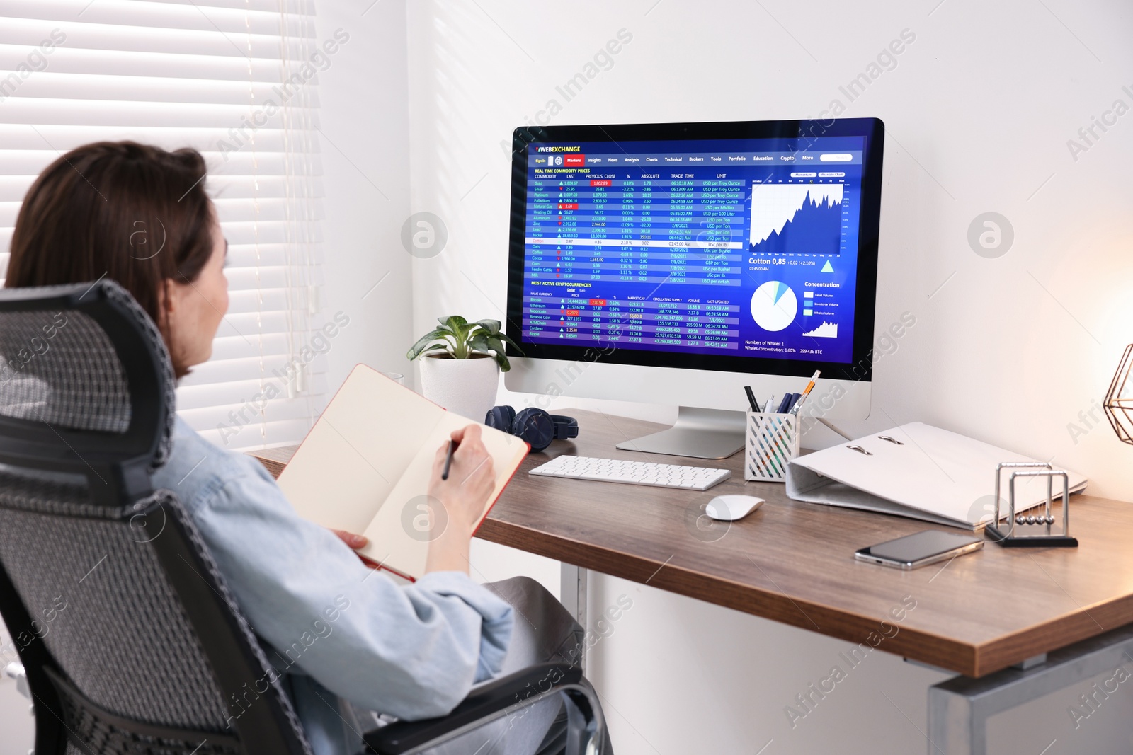 Photo of Stock exchange. Woman taking notes while analysing financial market on computer at wooden table indoors