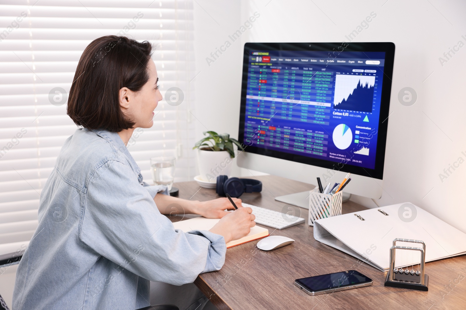 Photo of Stock exchange. Woman taking notes while analysing financial market on computer at wooden table indoors