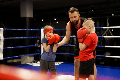 Photo of Children practicing fight on boxing ring under their coach supervision