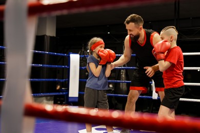 Children practicing fight on boxing ring under their coach supervision