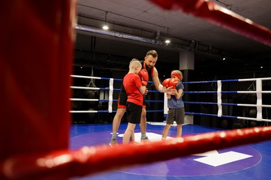 Children practicing fight on boxing ring under their coach supervision