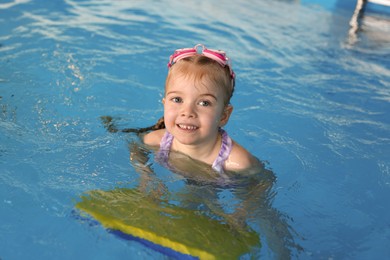 Little girl with goggles and kickboard swimming in pool indoors