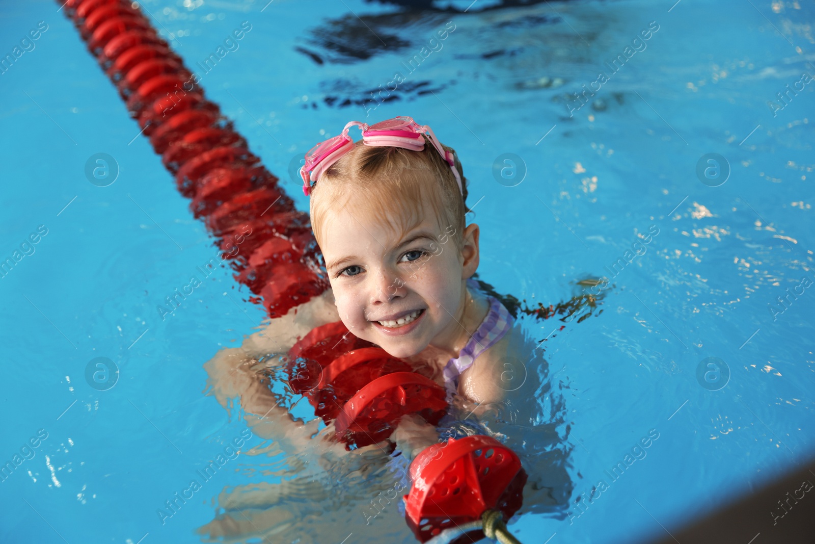 Photo of Little girl with goggles swimming in pool indoors