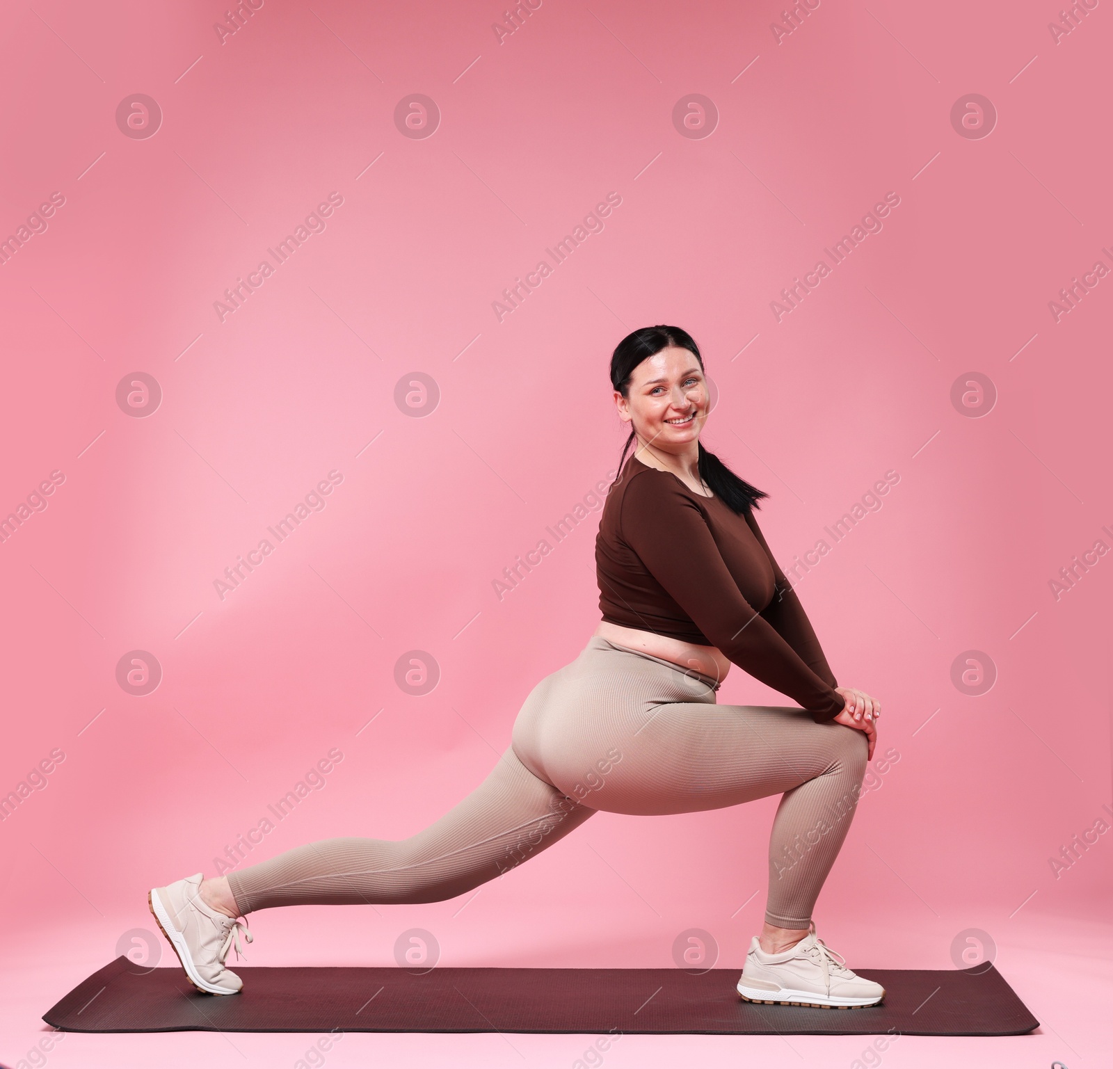 Photo of Plus size woman in gym clothes exercising on pink background