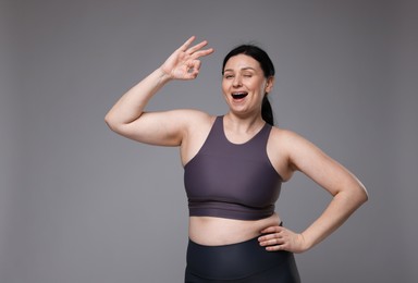 Photo of Plus size woman in gym clothes showing ok gesture on grey background