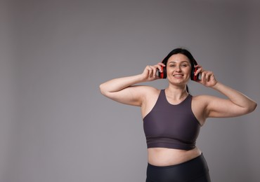 Plus size woman in gym clothes and headphones on grey background, space for text