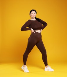 Plus size woman in gym clothes on orange background