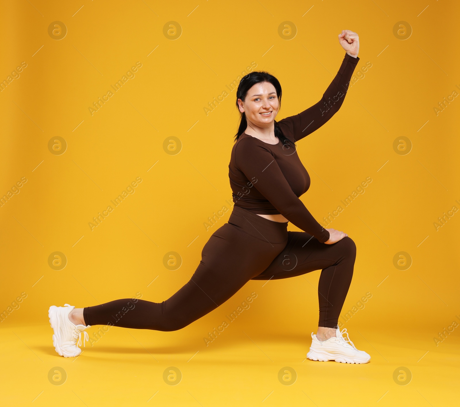 Photo of Plus size woman in gym clothes exercising on orange background