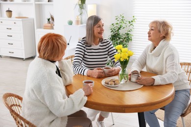 Friendship. Senior women enjoying hot drinks at table indoors