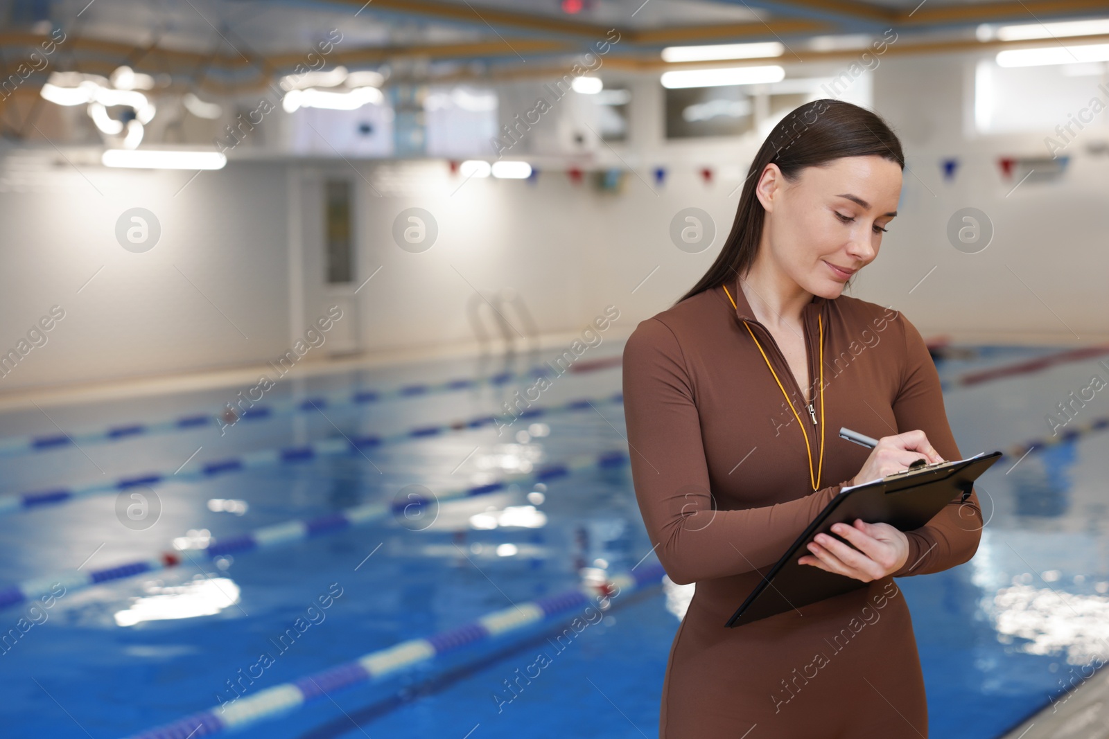 Photo of Swimming coach with whistle and clipboard at indoor pool. Space for text