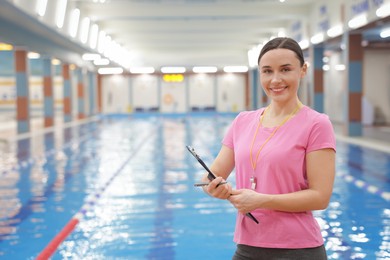 Swimming coach with whistle and clipboard at indoor pool. Space for text