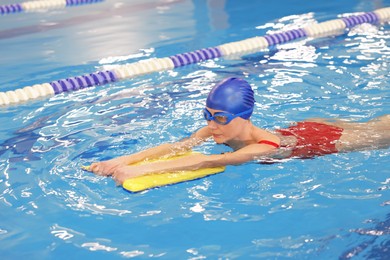 Young woman wearing cap and goggles with kickboard swimming in pool indoors