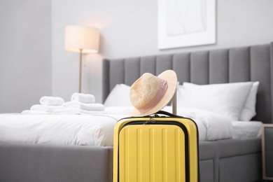 Suitcase with hat near bed in hotel room