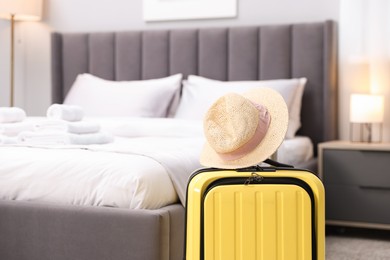 Suitcase with hat near bed in hotel room