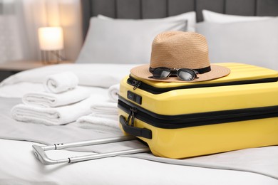 Photo of Suitcase with hat and sunglasses on bed in hotel room