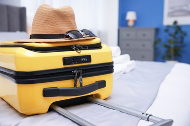 Suitcase with hat and sunglasses on bed in hotel room, closeup