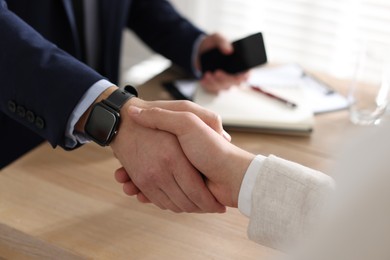 Photo of Men shaking hands at wooden table in office, closeup