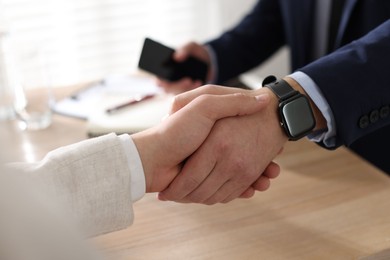 Photo of Men shaking hands at wooden table in office, closeup