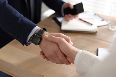 Photo of Men shaking hands at wooden table in office, closeup