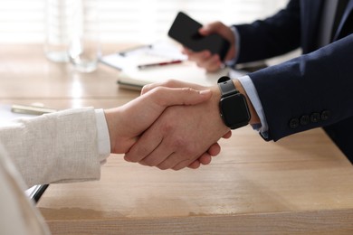 Photo of Men shaking hands at wooden table in office, closeup