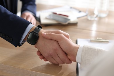 Photo of Men shaking hands at wooden table in office, closeup