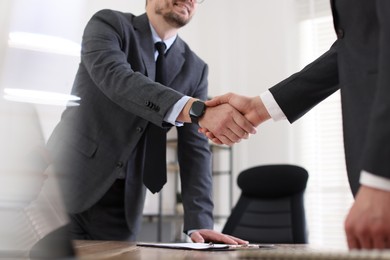 Photo of Men shaking hands at table in office, closeup