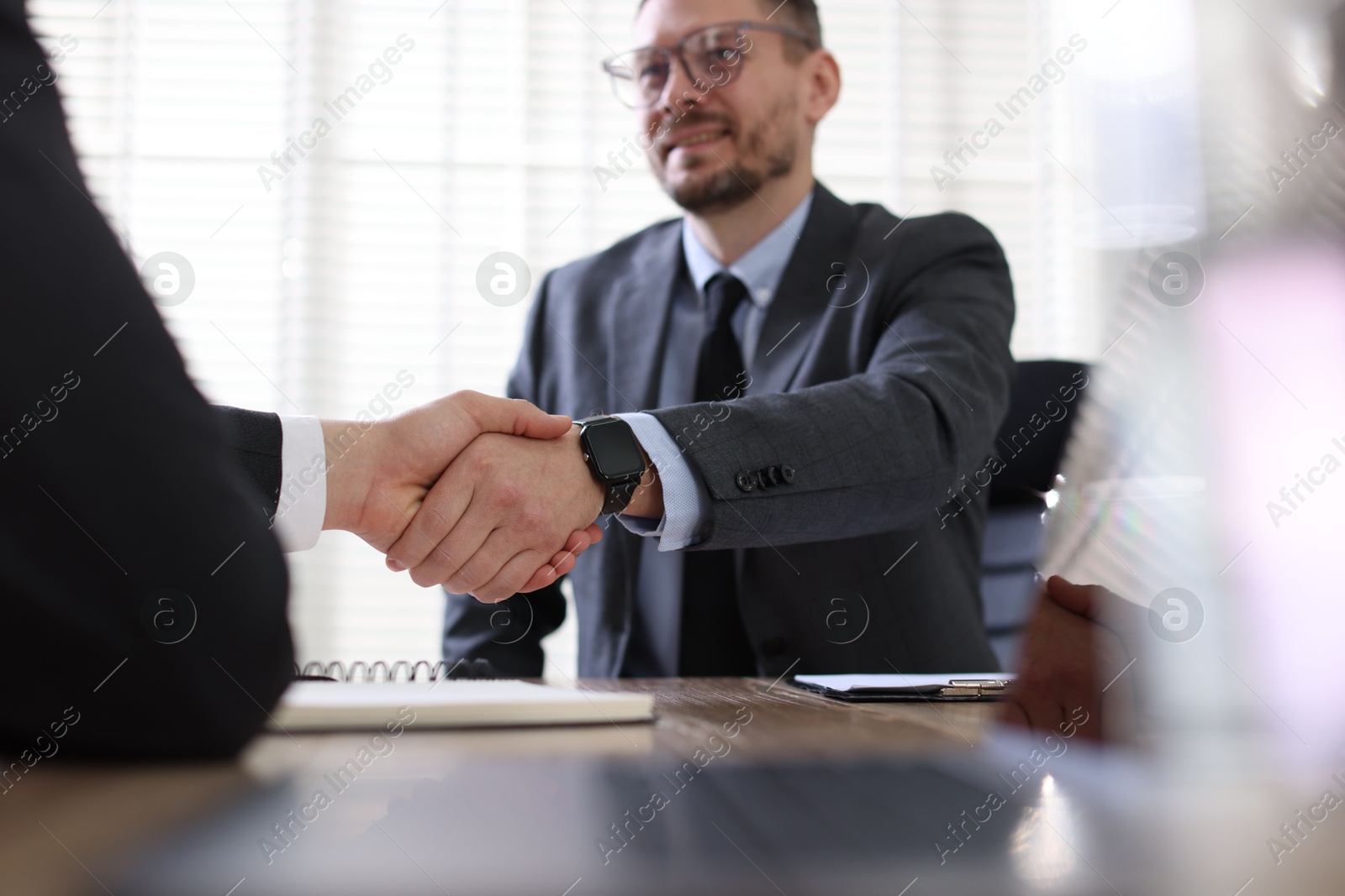 Photo of Men shaking hands at table in office, selective focus