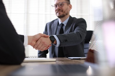 Photo of Men shaking hands at table in office, selective focus