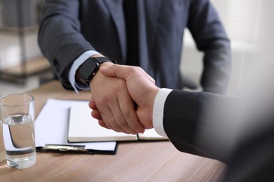 Photo of Men shaking hands at wooden table in office, closeup