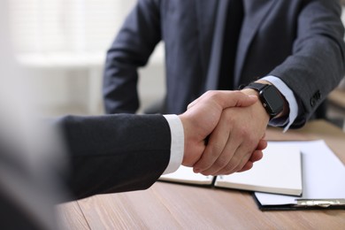 Photo of Men shaking hands at wooden table in office, closeup