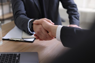 Photo of Men shaking hands at wooden table in office, closeup