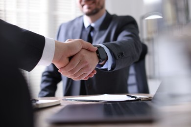 Men shaking hands at table in office, closeup