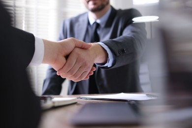 Men shaking hands at table in office, closeup