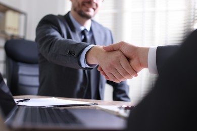 Men shaking hands at table in office, closeup