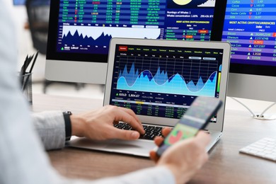 Photo of Financial trading specialist with smartphone and laptop at table in office, closeup