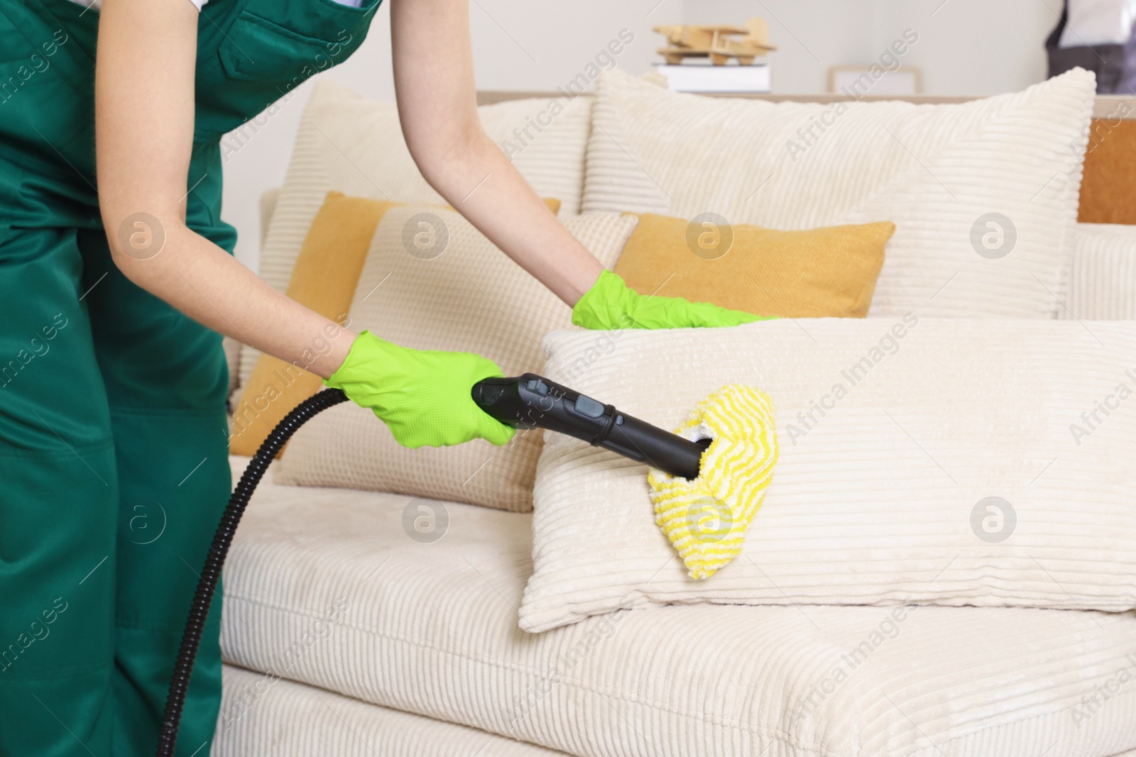 Photo of Professional janitor steam cleaning sofa in room, closeup