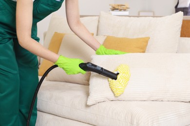 Professional janitor steam cleaning sofa in room, closeup