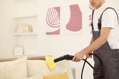 Photo of Professional janitor steam cleaning sofa in room, closeup