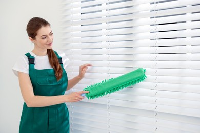 Professional janitor cleaning dust off window blinds indoors