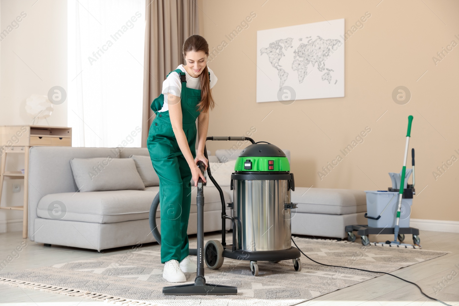 Photo of Professional cleaning service worker vacuuming rug indoors