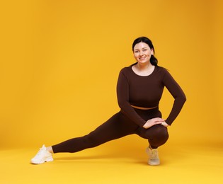 Plus size woman in gym clothes exercising on orange background