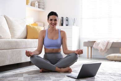 Woman with laptop meditating on floor at home