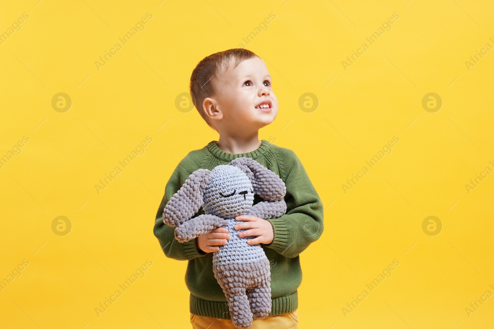 Photo of Cute little boy with toy bunny on yellow background