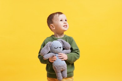 Cute little boy with toy bunny on yellow background