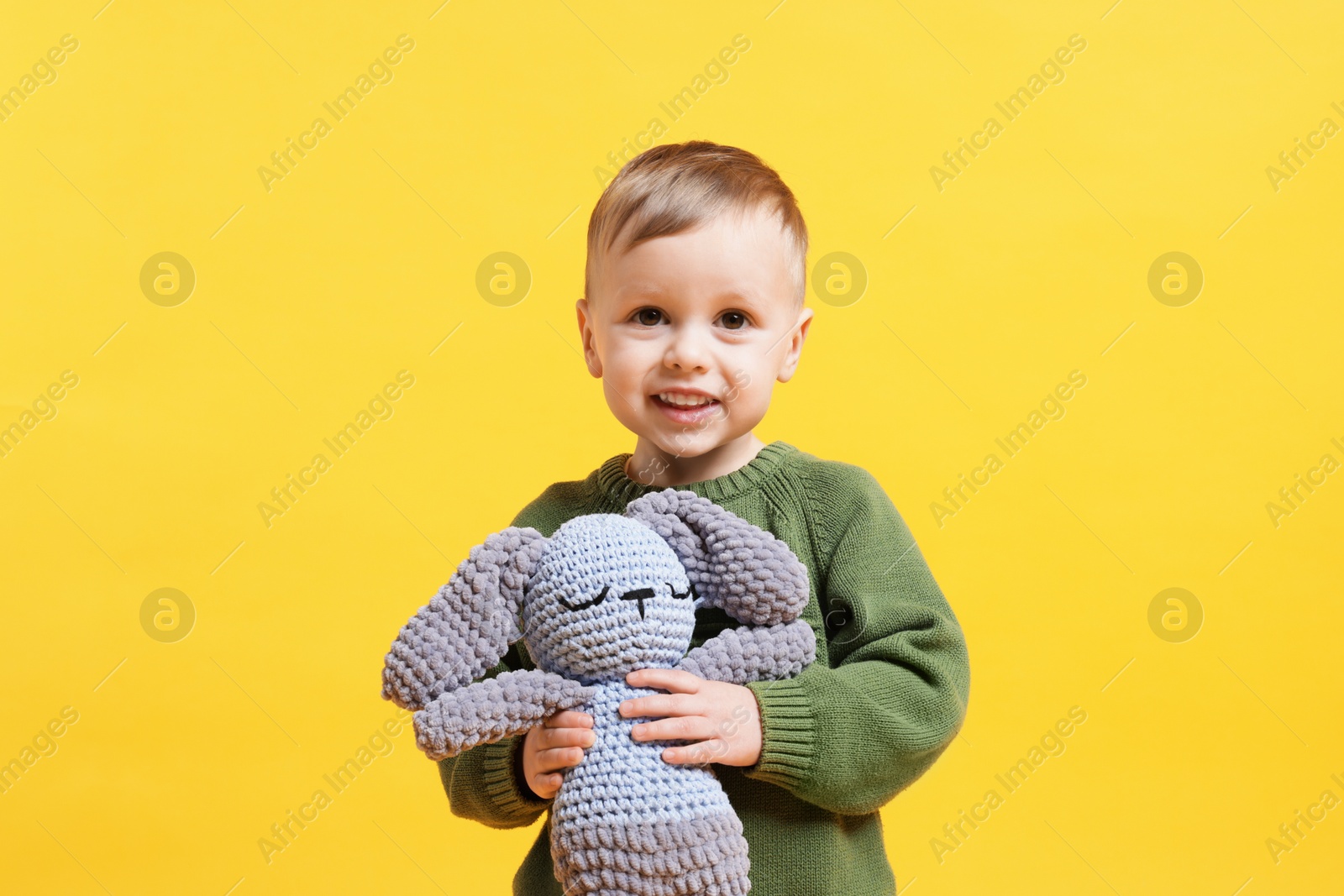 Photo of Cute little boy with toy bunny on yellow background